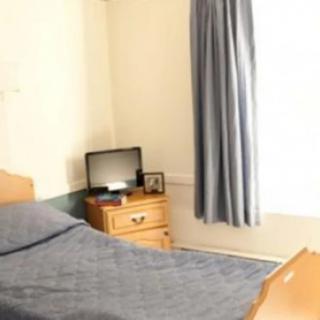 A simple bedroom with a bed, nightstand, and a small TV.