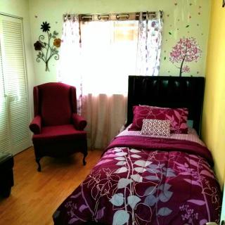 A cozy bedroom featuring a single bed with floral bedding and a maroon armchair.
