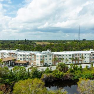 Aerial view of a modern building surrounded by lush greenery and a small body of water.