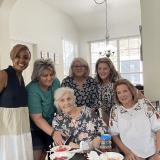 A group of women gathered together, smiling for a family photo indoors.