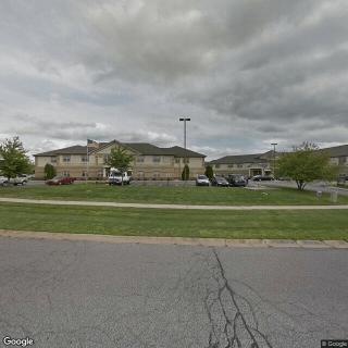A view of a building with a parking lot and cars under a cloudy sky.