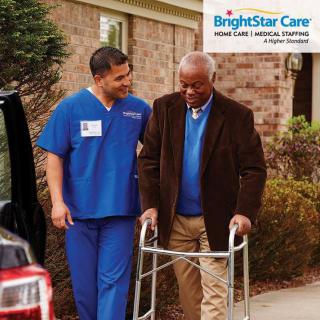 A caregiver assisting an elderly man using a walker outdoors.