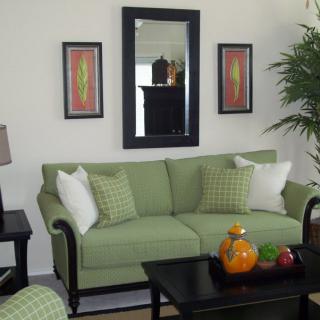 A cozy living room with a green sofa, decorative pillows, a wall mirror, and artwork. A coffee table with decorative items is in front of the sofa.