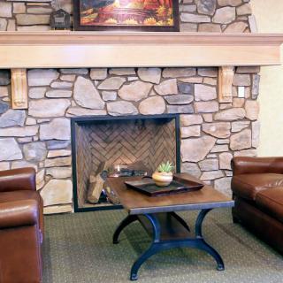 A cozy living room featuring a stone fireplace flanked by leather chairs and a central coffee table.