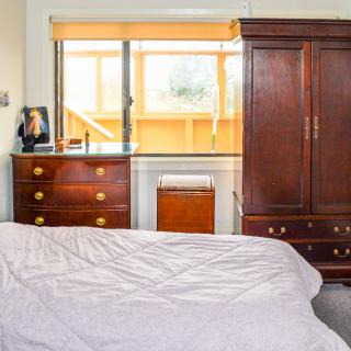 A cozy bedroom featuring a wooden wardrobe and dresser by a sunlit window.