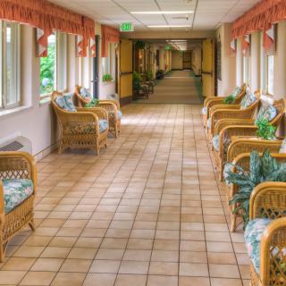 A long hallway with wicker chairs and a tiled floor, lined with windows.