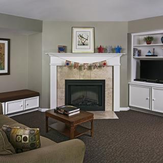 A cozy living room featuring a fireplace with a garland, a television on built-in shelves, and comfortable seating.