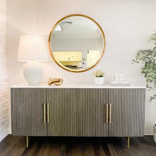 A stylish mid-century modern sideboard with a round mirror, decorative items, and a table lamp in a minimalist setting.