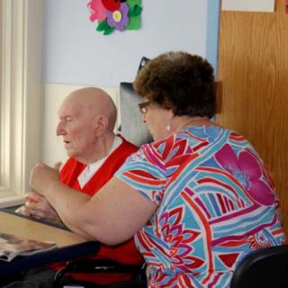 An elderly person receiving assistance from a caregiver in a nursing home setting.