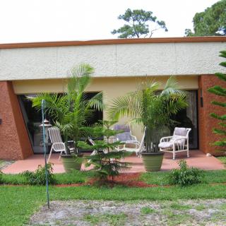A cozy patio with chairs and lush greenery in front of a modern house.
