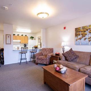 A cozy living room and kitchen area with a sofa, armchair, and coffee table in an open-plan apartment.