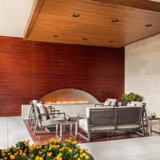 A modern outdoor patio with comfortable seating and a cozy fireplace, surrounded by stylish wood paneling.
