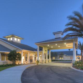 A well-lit building entrance with palm trees and a circular driveway in the evening.