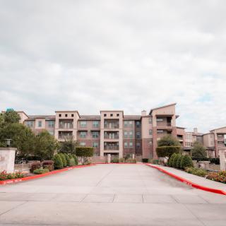 A modern apartment building with a wide driveway under a cloudy sky.