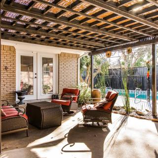 A cozy outdoor patio with comfortable seating under a pergola, overlooking a pool.