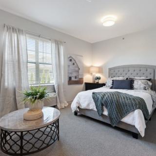 A cozy bedroom with modern decor, featuring a comfortable bed, a bedside lamp, and a window letting in natural light.