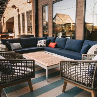 A stylish outdoor patio setup with wicker chairs and a large sectional sofa around a wooden coffee table.
