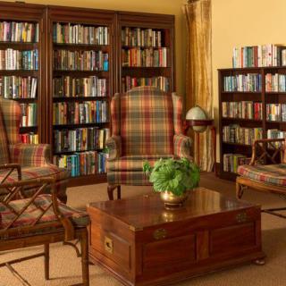 A cozy library setting with bookshelves, a plaid armchair, and a wooden coffee table featuring a small indoor plant.