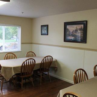 A dining room with several tables and chairs, featuring paintings on the walls and a window providing natural light.