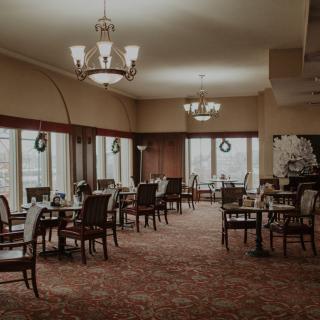 An elegant, empty dining room with chandeliers and neatly arranged tables and chairs.