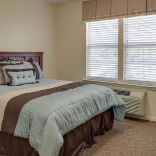 A cozy bedroom with a neatly made bed and large window blinds.