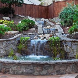 A beautiful garden waterfall with stone walls and lush greenery.