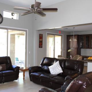 A spacious living room with leather sofas, a ceiling fan, and a view into the kitchen.