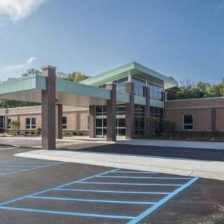 A modern building with a covered entrance and an adjacent parking area.