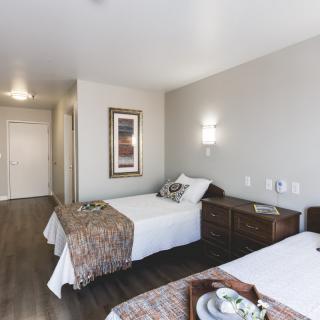A modern hotel room featuring twin beds with elegant decor and wooden flooring.