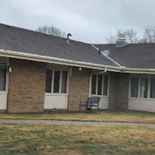 A view of a brick residential building with a bench in front and cloudy skies overhead.