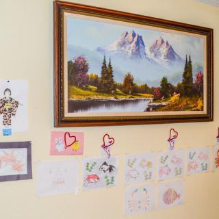 A wall decorated with a mountain landscape painting and children's drawings.