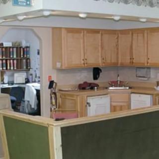 A kitchen area adjacent to an office space featuring wooden cabinets and a bookshelf.