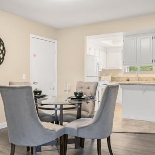 A modern dining area with a glass table and upholstered chairs, seamlessly connected to a bright kitchen.