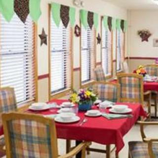 A colorful dining area with tables set for a meal, featuring bright red tablecloths, checkered chairs, and decorative window treatments.