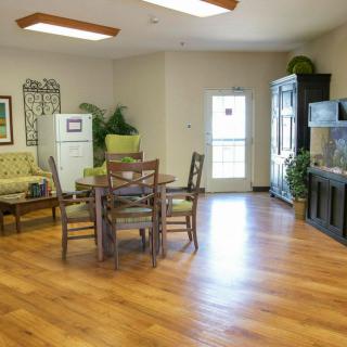 A cozy living room with hardwood flooring, featuring a dining table and chairs, indoor plants, and a television.