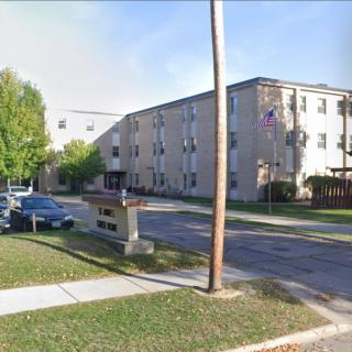An apartment complex with parked cars along a street lined with trees and sidewalks.