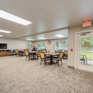 A spacious dining area with tables and chairs, featuring large windows that allow natural light to fill the room.
