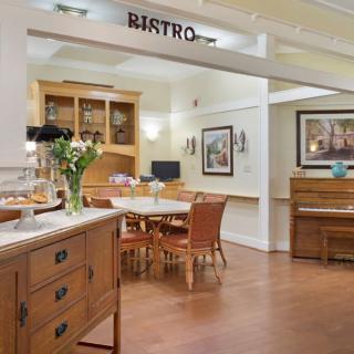 A cozy bistro interior featuring a dining area with wooden furniture, a piano, and decorative flowers.
