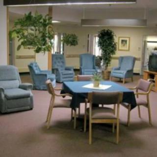 A spacious waiting room with comfortable chairs and a central table, surrounded by potted plants.