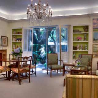 A beautifully decorated living room with traditional furnishings, a chandelier, and large windows opening to a garden view.