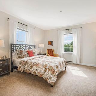 A cozy bedroom featuring a patterned bedspread, two windows with curtains, and warm lighting.