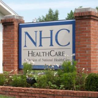 A sign for NHC HealthCare displayed on a brick structure with surrounding greenery.