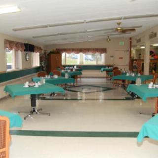 An empty dining hall with tables covered in green tablecloths, prepared for guests.