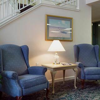 A cozy living room setup with blue armchairs, a lamp on a side table, and artwork on the wall.