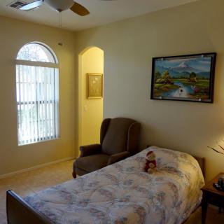 A cozy bedroom with a single bed, an armchair, a window with blinds, and a painting on the wall.