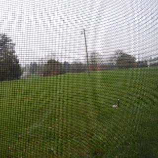 A grassy field on an overcast day, viewed through a mesh screen.
