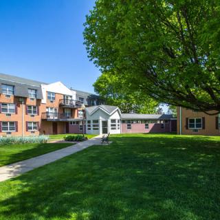 A residential apartment building with a grassy lawn and pathway on a sunny day.