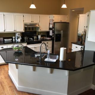 A modern kitchen with white cabinetry, black countertops, and stainless steel appliances.