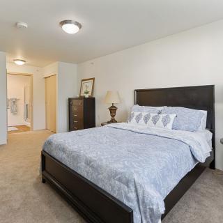 A spacious bedroom with a neatly made bed, dark wood furniture, and neutral decor.