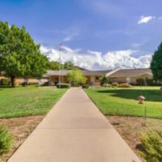 A beautiful pathway leading to a building surrounded by green lawns and trees under a blue sky with clouds.